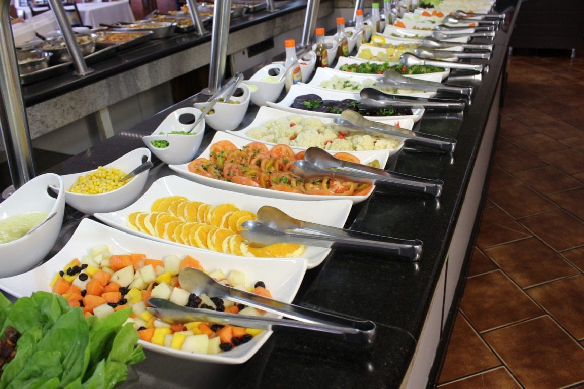Travessas de saladas, frutas e conservas no balcão refrigerado