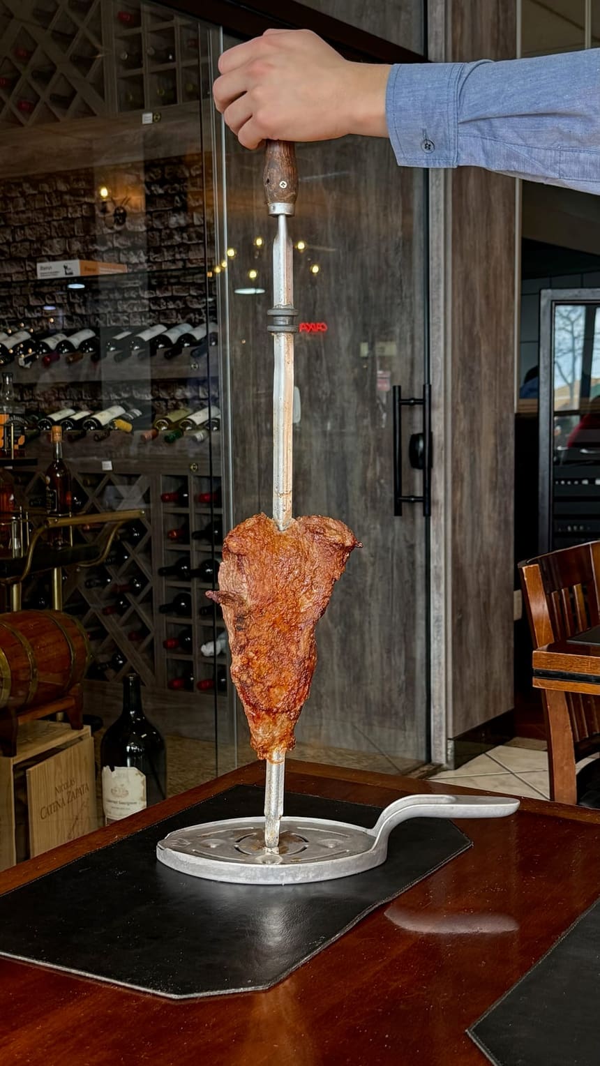 Espeto de carne servido na mesa, com a adega da casa ao fundo