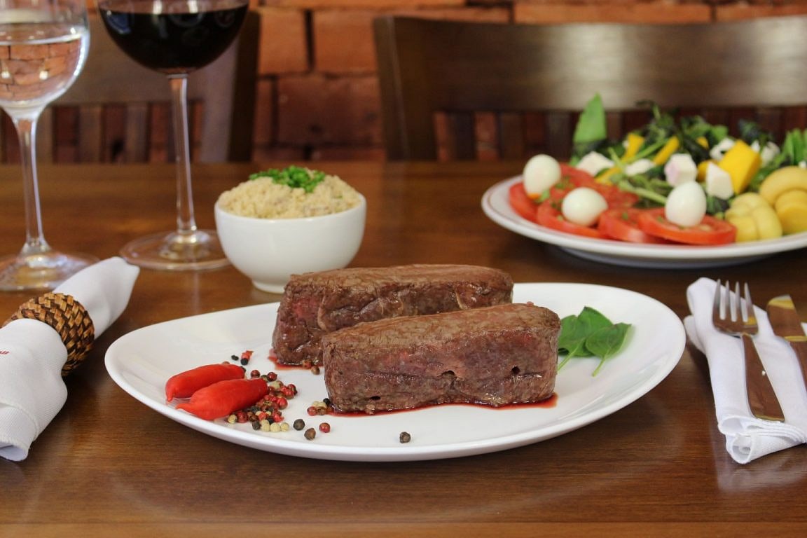 Corte nobre servido no prato, com acompanhamentos e salada na mesa do Grill Hall