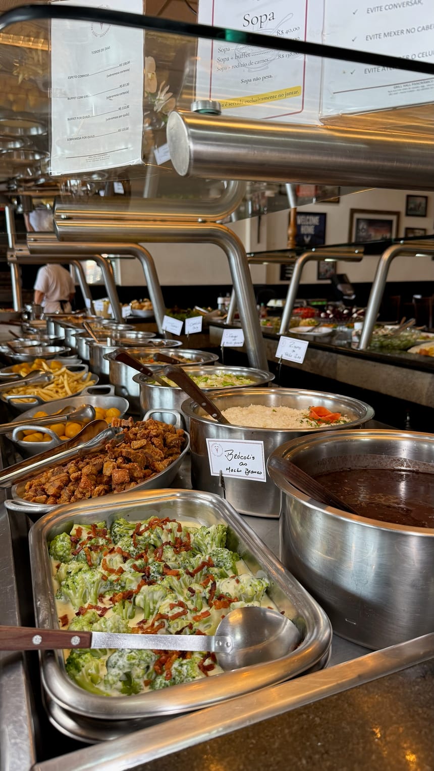 Balcão do buffet com brócolis, torresmo, arroz e acompanhamentos