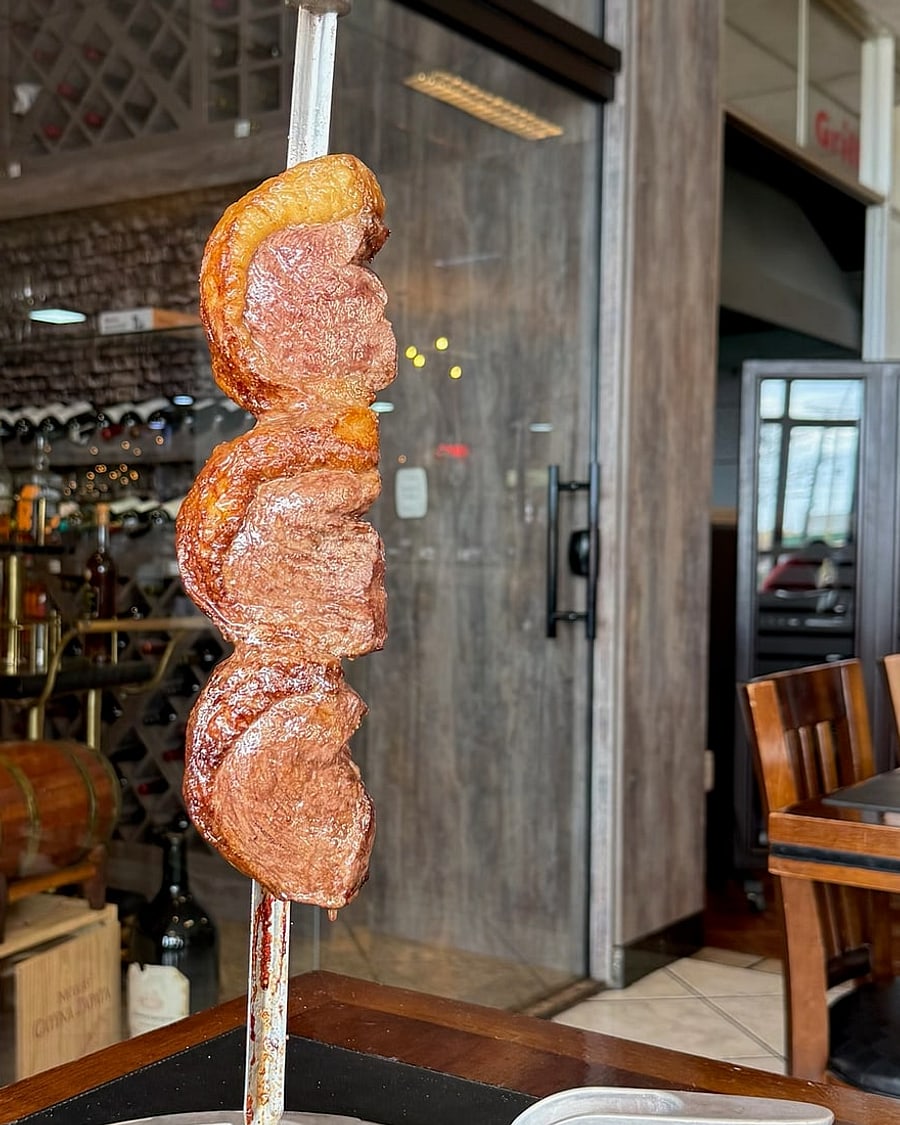 Espeto com três cortes de carne assados, servido com a adega da casa ao fundo